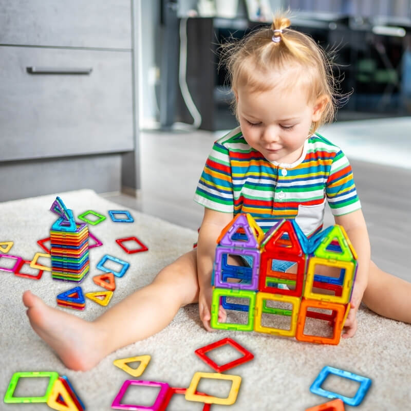 une-petite-fille-construit-des-maisons-avec-ses-blocs-sur-un-tapis-blanc