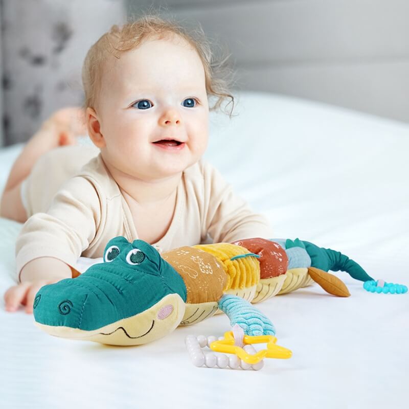 un-bebe-fille-joyeuse-souriante-couchee-sur-un-lit-avec-une-peluche-crocodile-coloree