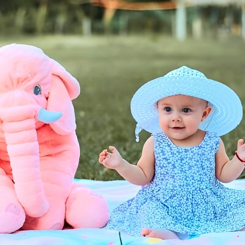 bebe-fille-avec-robe-bleue-et-chapeau-sur-une-nappe-avec-sa-peluche-elephant-rose