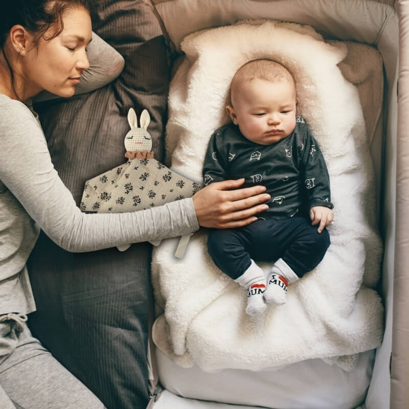 une-maman-dort-a-cote-de-son-bebe-qui-est-sur-un-cocon-douillet-blanc