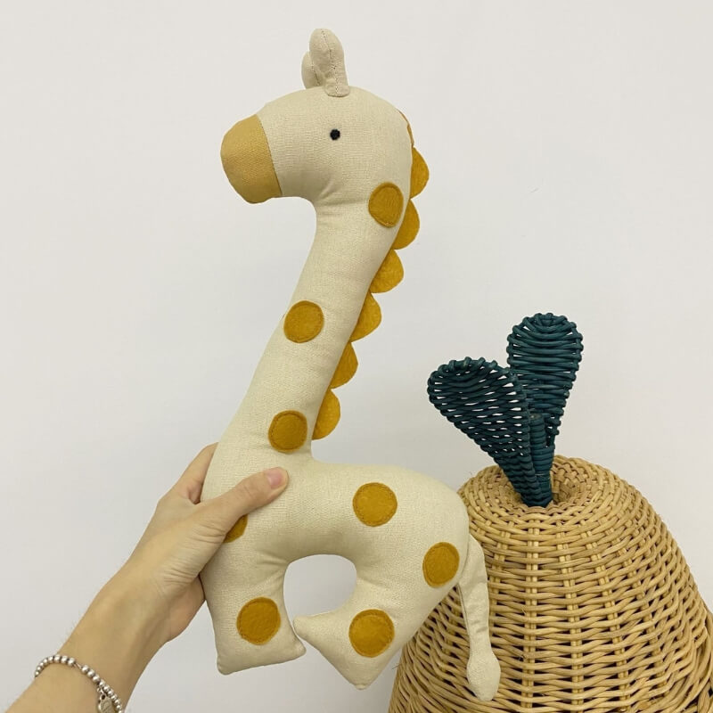 girafe-en-peluche-beige-tachetee-orange-tenune-dans-les-airs-a-cote-d_un-panier-en-osier