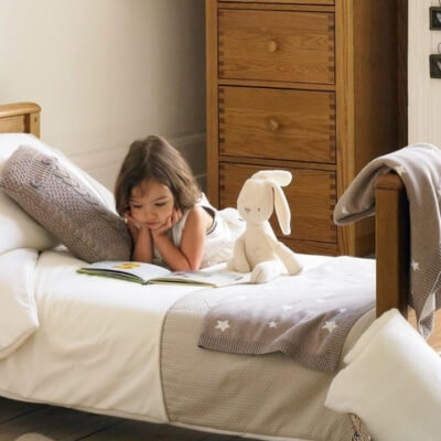 Une-fillette-de-7-ans-qui-lit-un-livre-couchée-sur-son-lit-avec-sa-peluche-lapin-blanche