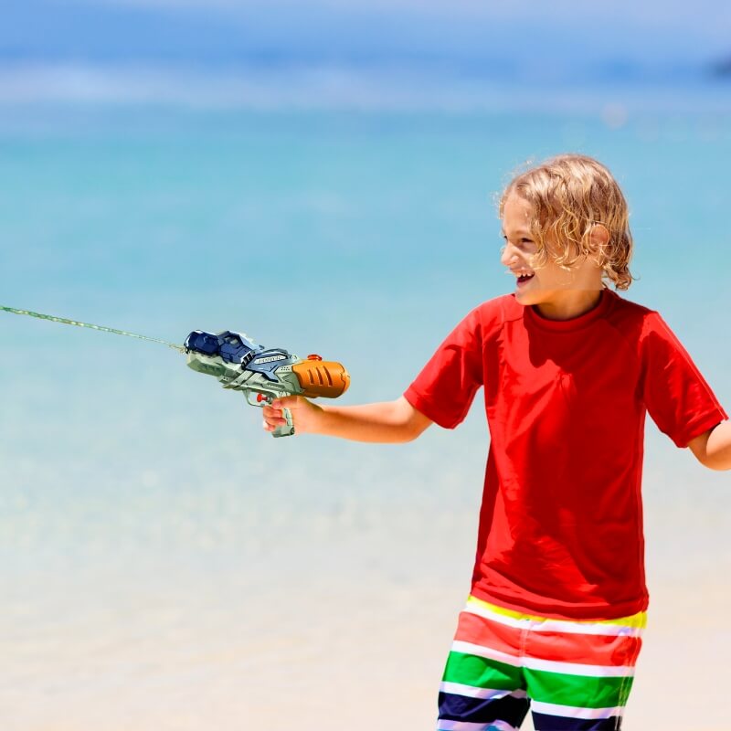 un-enfant-à-la-plage-heureux-avec-pistolet-a-eau-dinosaure-vacances